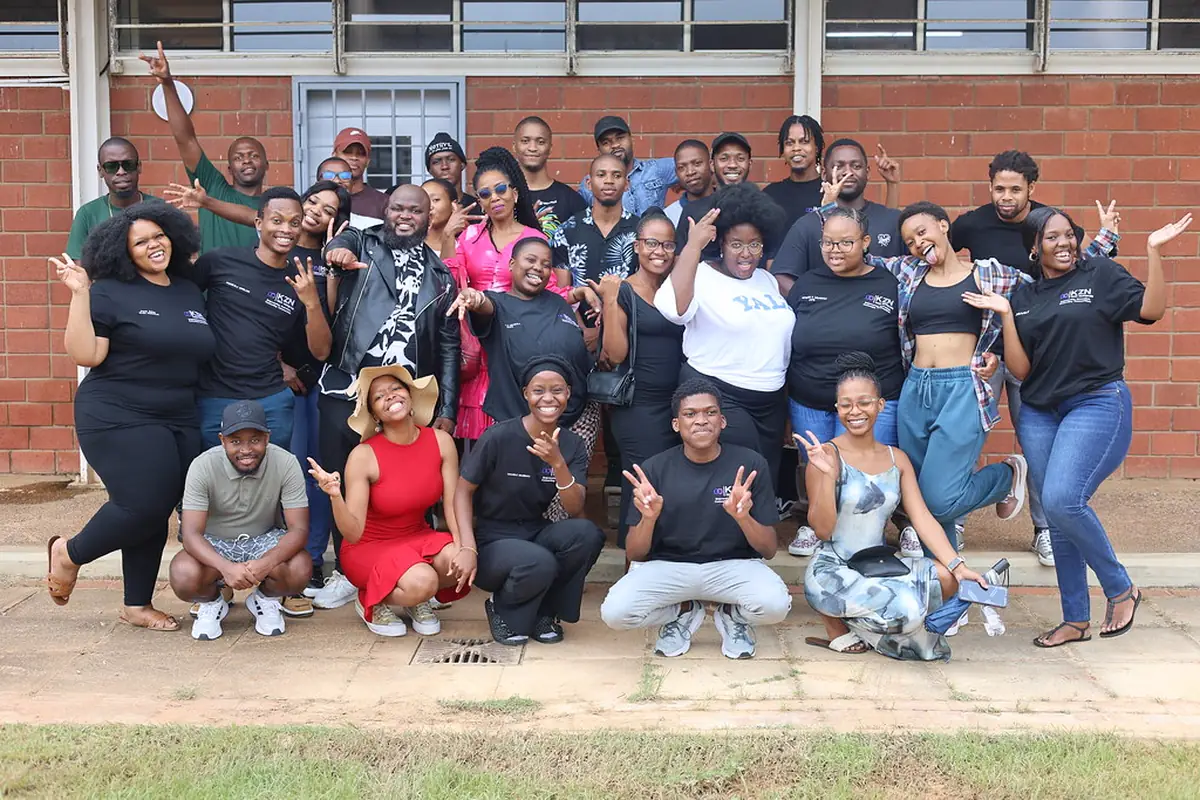 A large group of young people from the Tech Horizons community, smiling and waving outside a campus building.